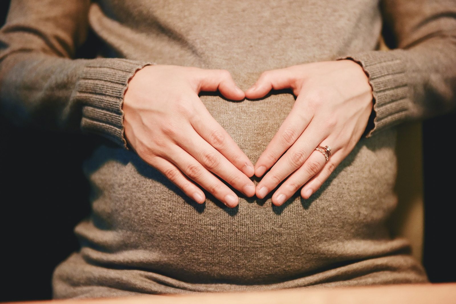 Pregnant woman holding hands in heart on belly