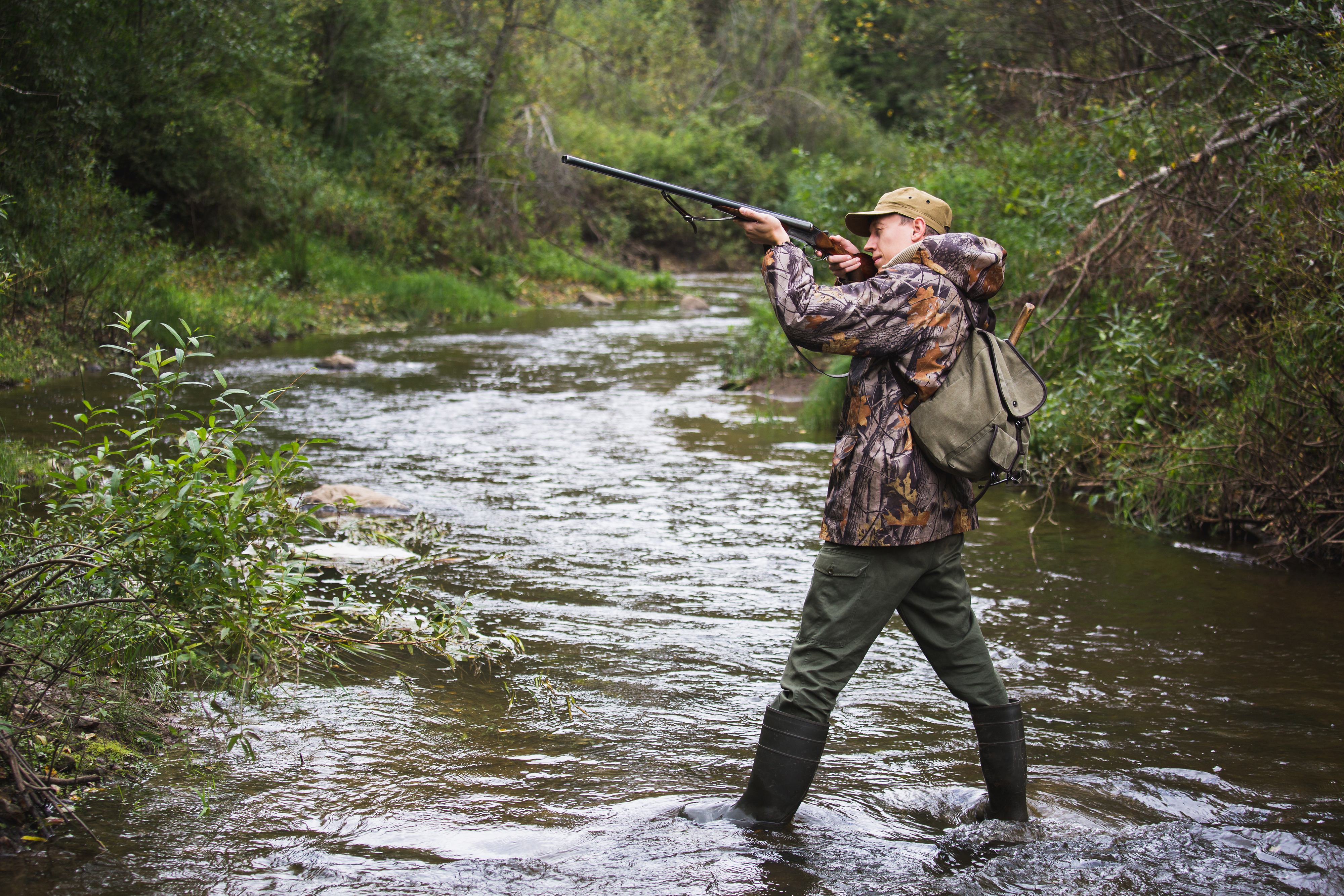 Hunter holding his gun standing on a creek