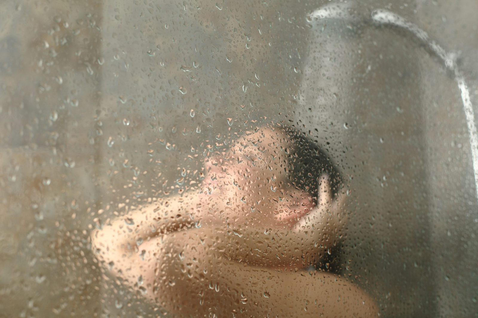Unfocused woman showering through the bath screen with water drops