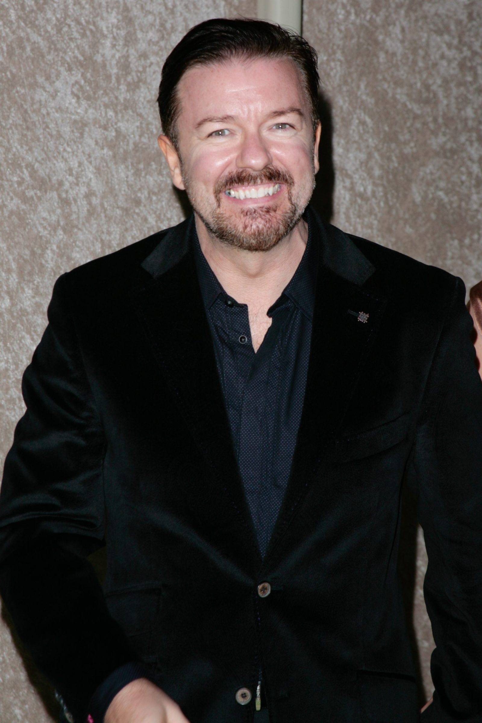 Ricky gervais smiling in a black suit