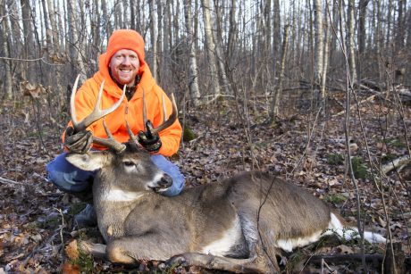 Hunter in orange holding up a deer that he killed